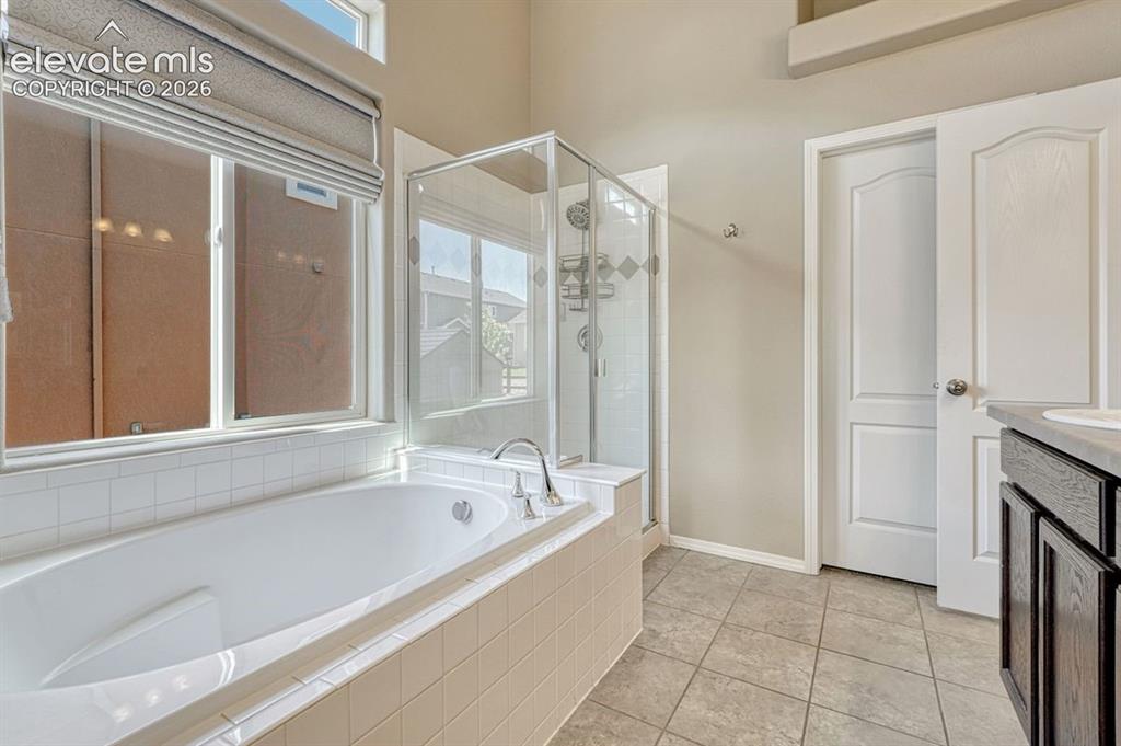 Image 27 of 50: Soaking tub with white tile surround, glass-enclosed shower, dual windows w