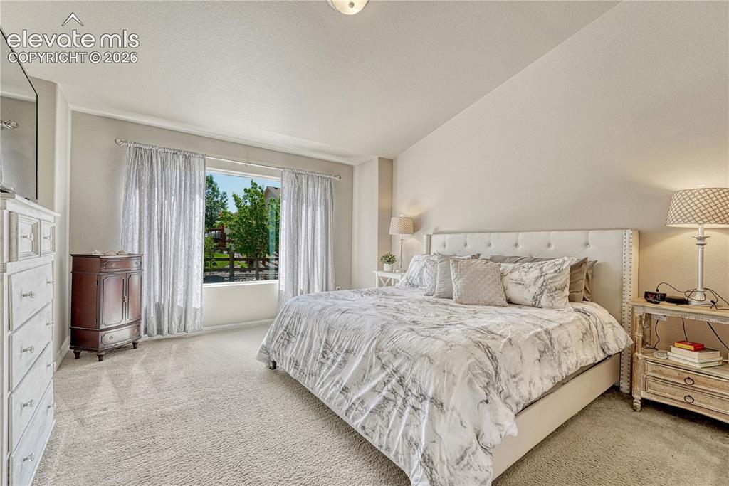 Image 4 of 50: Primary Bedroom with vaulted ceilings, carpet and ensuite bath