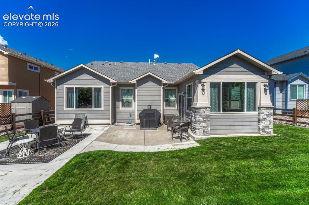 Image 41 of 50: Rear exterior featuring a concrete patio, a manicured lawn, and a shed