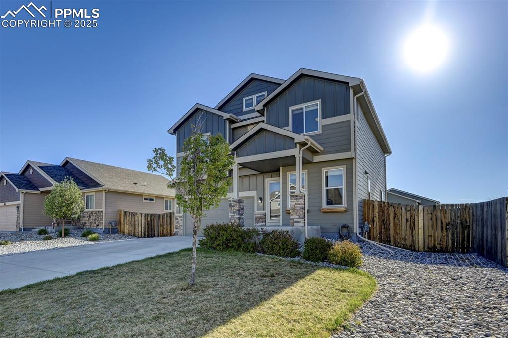 Caption: View of front of house with fence, board and batten siding, concrete driveway, and a garage