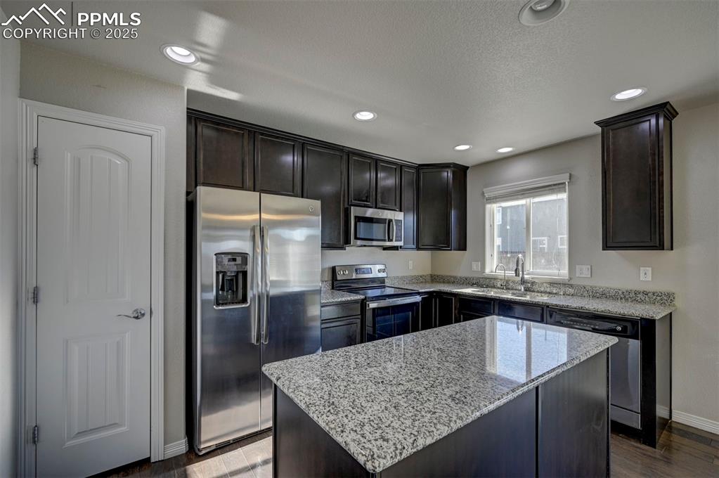 Image 18 of 50: Kitchen with a sink, a kitchen island, light stone countertops, and stainle