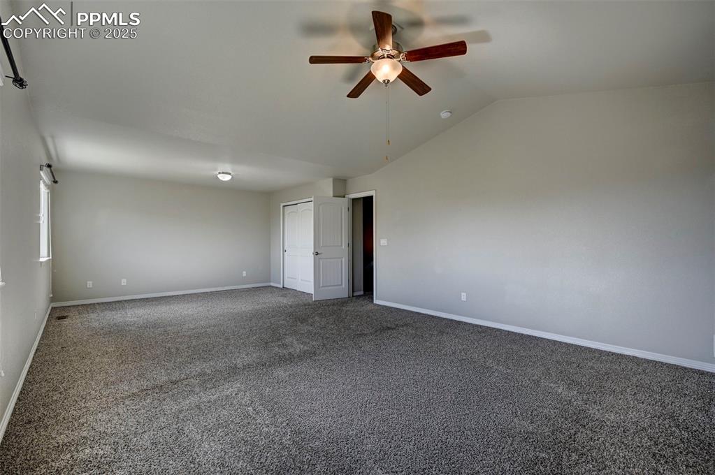 Image 25 of 50: Carpeted empty room featuring baseboards, ceiling fan, and lofted ceiling