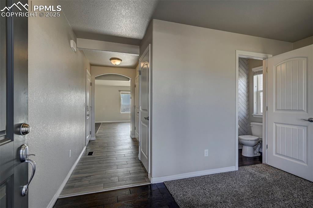 Image 6 of 50: Hallway with arched walkways, baseboards, dark wood-style flooring, and a t