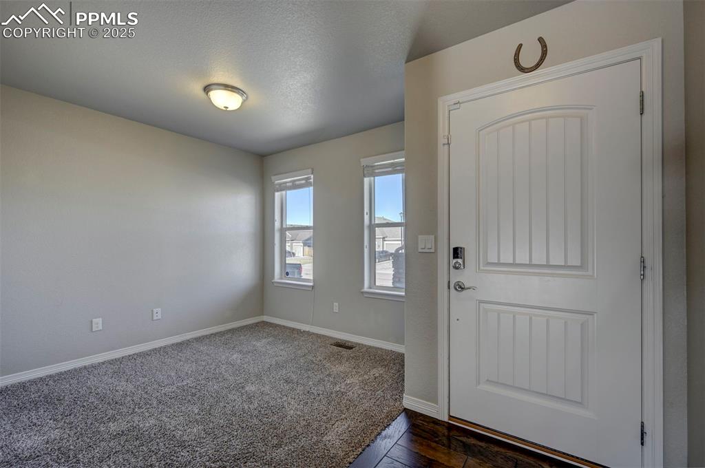 Image 7 of 50: Entrance foyer featuring baseboards, dark colored carpet, a textured ceilin