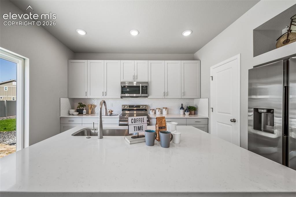 Image 14 of 21: Kitchen featuring an oversized island with a white countertop, stainless st
