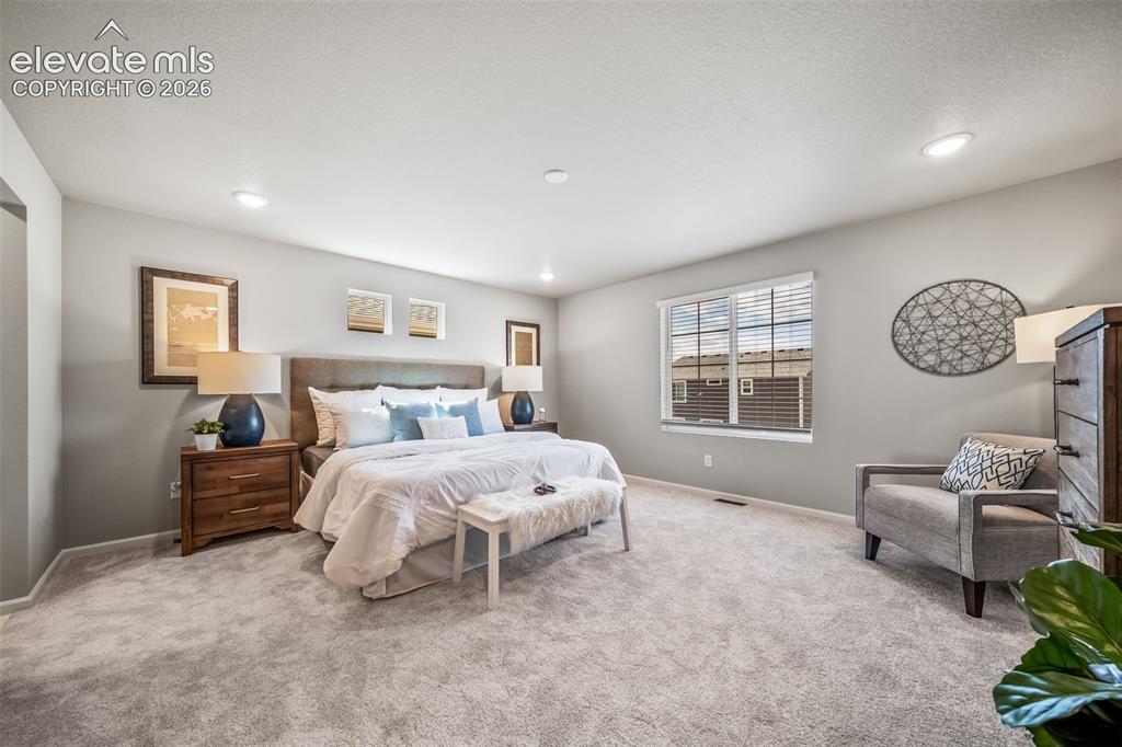 Image 19 of 21: Spacious bedroom featuring light gray carpeting, recessed lighting, and a l