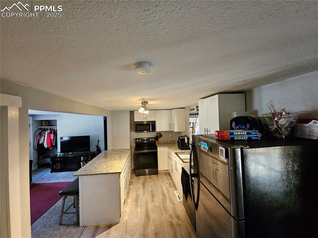 Image 10 of 23: Kitchen featuring stainless steel appliances, a textured ceiling, white cab