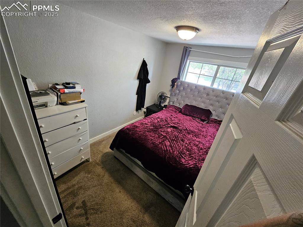 Image 11 of 23: Bedroom with dark carpet, a textured wall, and a textured ceiling