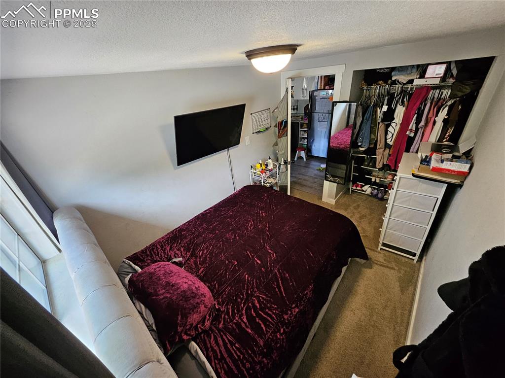 Image 12 of 23: Bedroom with carpet floors, a textured ceiling, and freestanding refrigerat