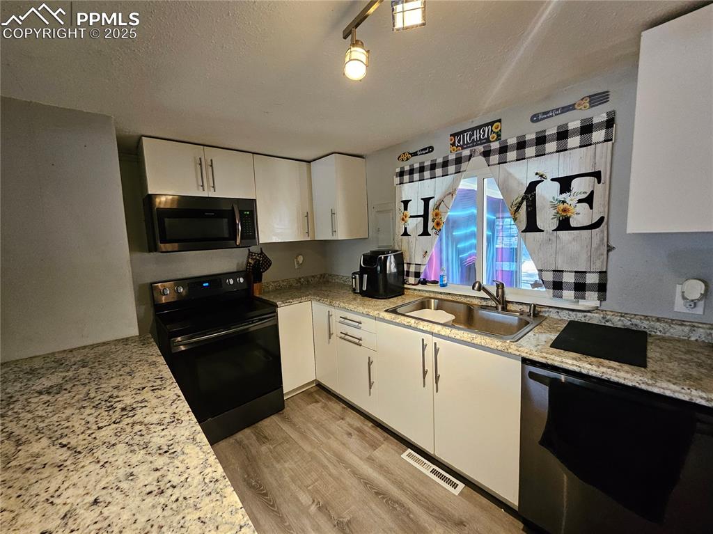 Image 8 of 23: Kitchen featuring black stove, dishwasher, white cabinetry, light stone cou