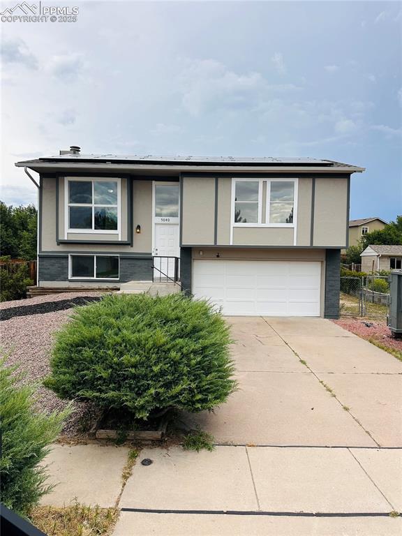 Caption: View of front facade with driveway, a garage, roof mounted solar panels, and stucco siding