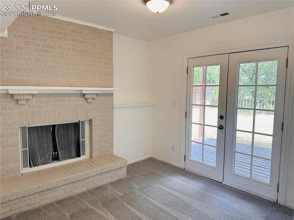 Image 8 of 11: Unfurnished living room featuring french doors, carpet flooring, and a fire
