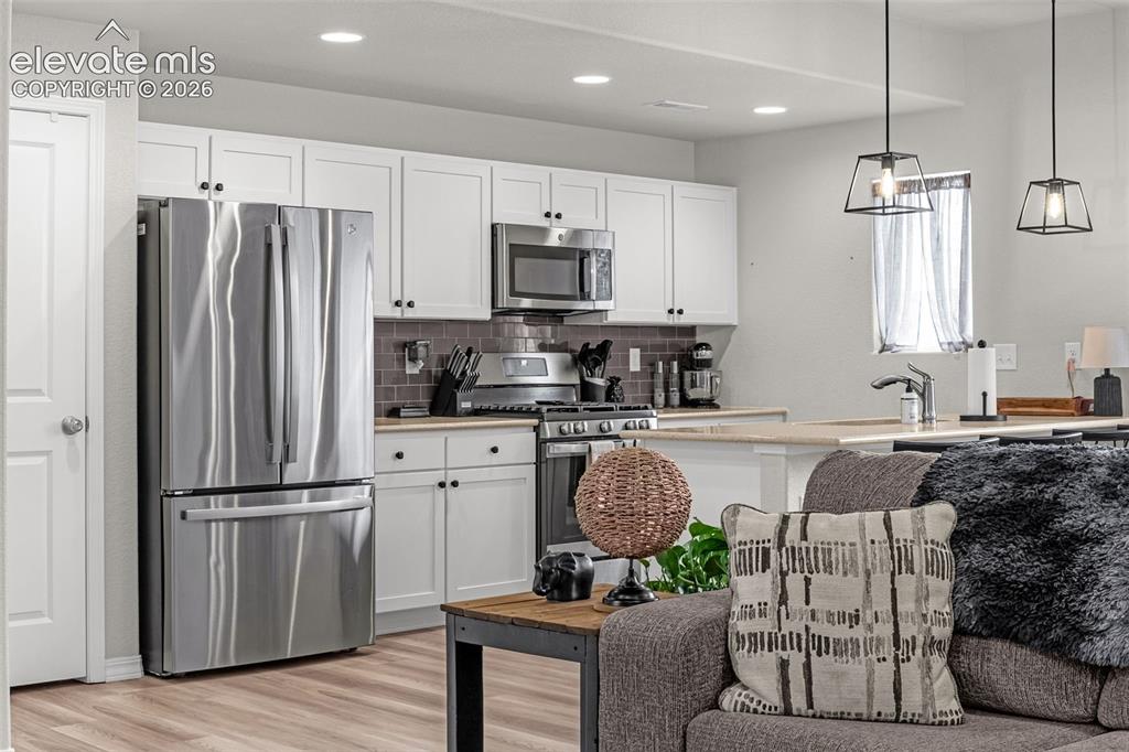 Image 3 of 46: Open-concept living space featuring a kitchen with white cabinetry, stainle