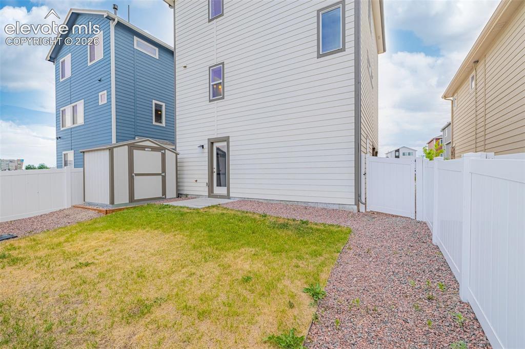 Image 5 of 46: Rear exterior featuring a privacy fence, gravel pathway, and a storage shed