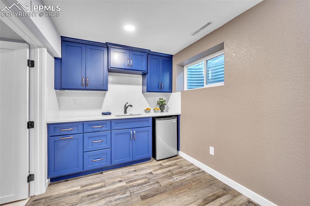 Image 28 of 49: Bar with a textured wall, blue cabinets, light wood-type flooring, stainles