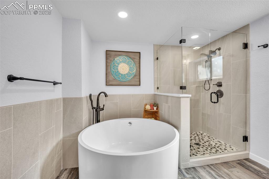 Image 35 of 49: Bathroom featuring a soaking tub, tile walls, a stall shower, wood finished