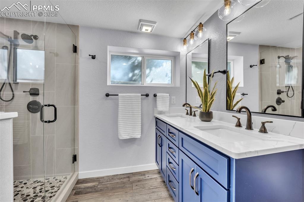 Image 36 of 49: Bathroom with double vanity, a textured ceiling, a shower stall, light wood