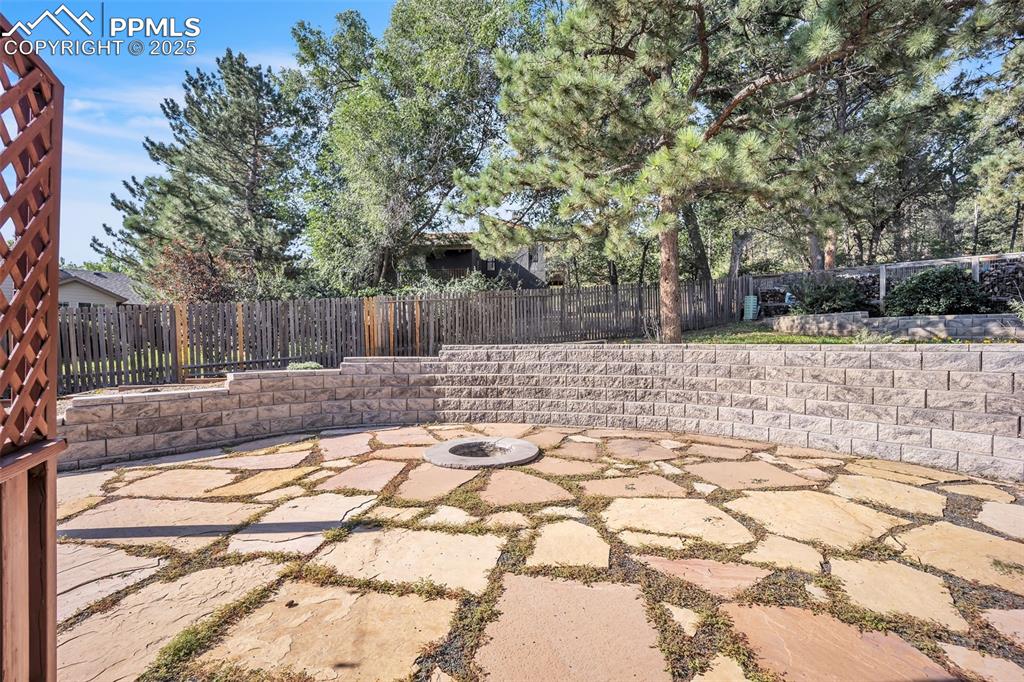 Image 41 of 49: Fenced backyard with an outdoor fire pit and a patio area