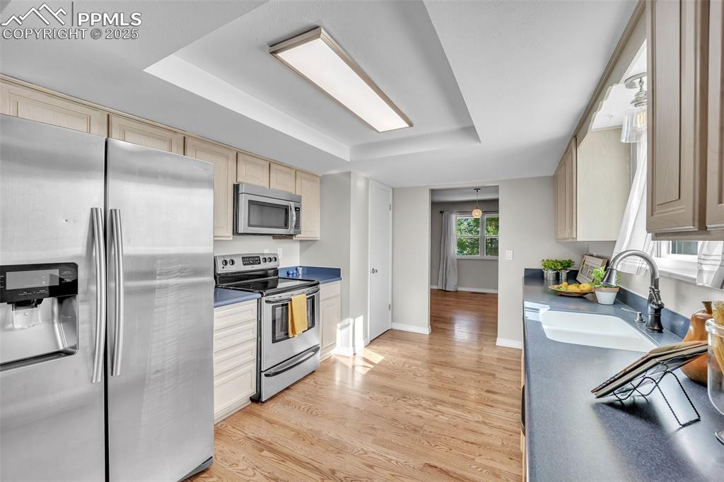 Image 8 of 49: Kitchen with stainless steel appliances, light wood-style floors, dark coun