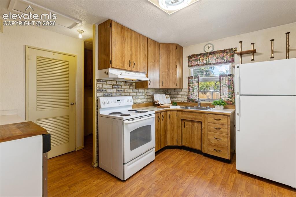 Image 14 of 45: Kitchen featuring wood-finish cabinetry, white appliances, and a brick-look