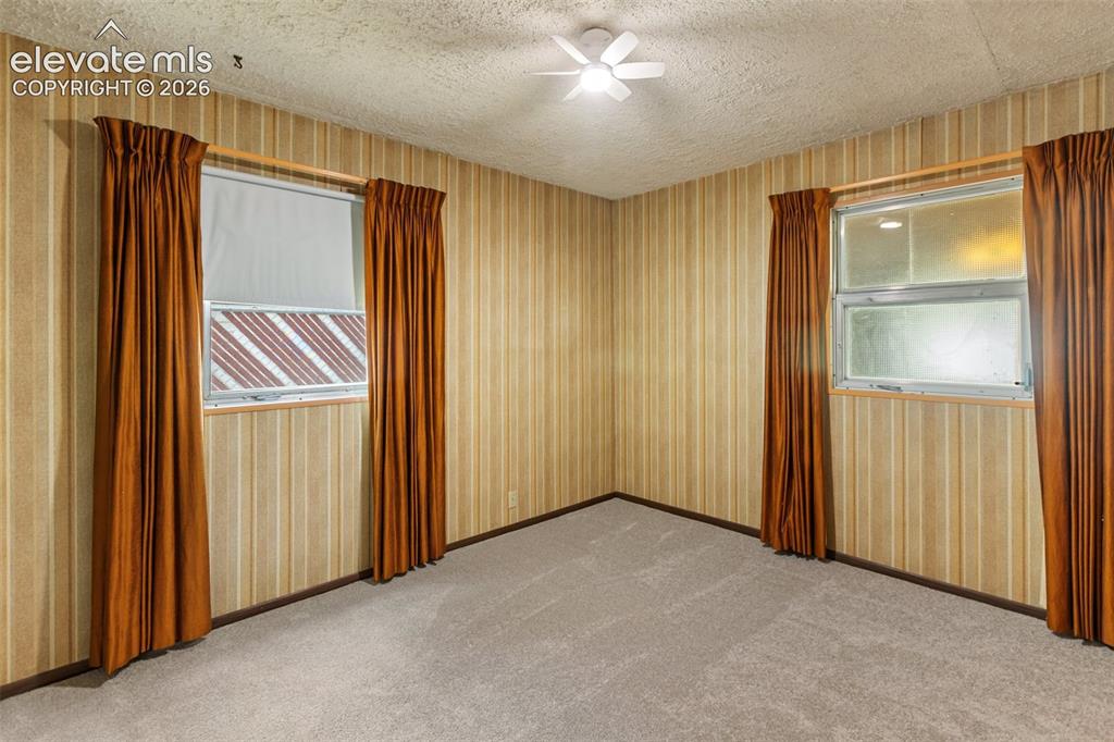 Image 20 of 45: Textured ceiling with a ceiling fan, striped wallpaper, and two windows wit