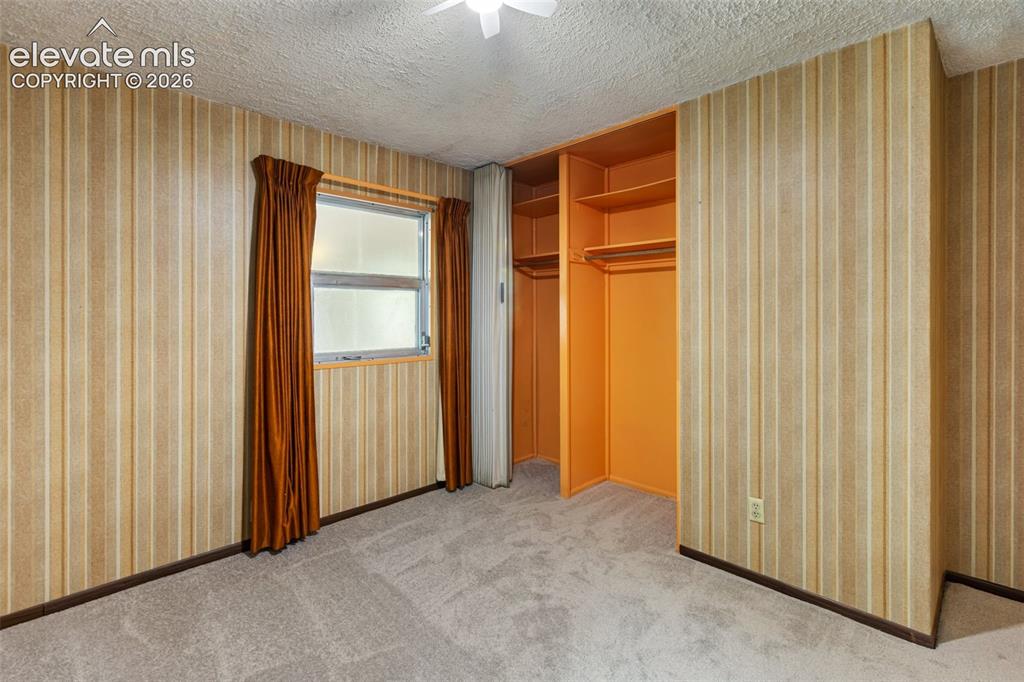 Image 21 of 45: Soft gray carpeting, window with a wood-finish frame, textured ceiling, bui