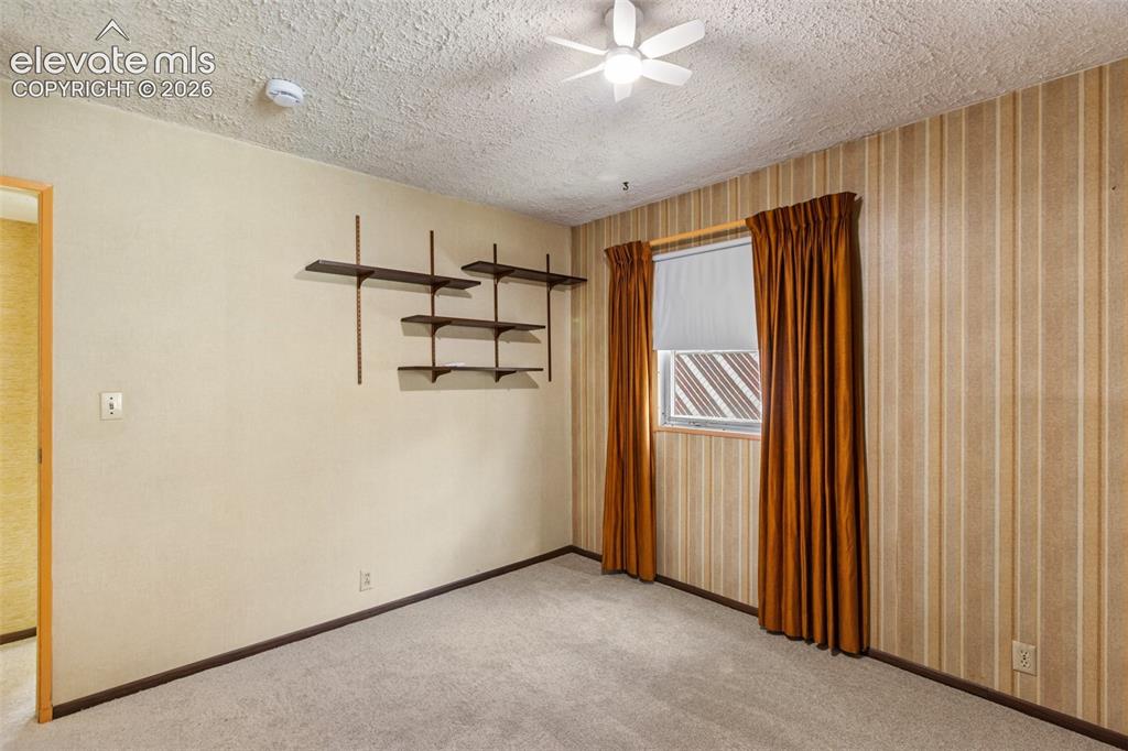 Image 22 of 45: Carpeted flooring, built-in shelving, window with blinds, ceiling fan
