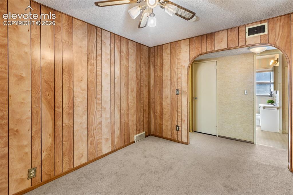 Image 28 of 45: Wood paneling walls, neutral tone carpeting, arched doorway, ceiling fan wi