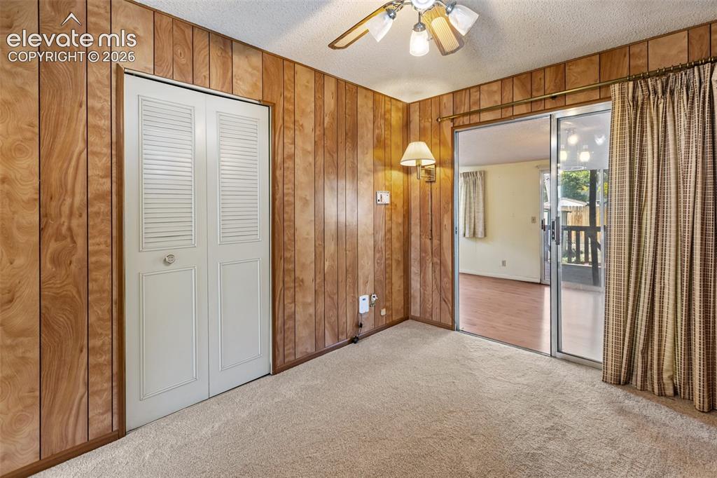 Image 29 of 45: Textured carpeting, wood paneling, louvered bi-fold closet doors, wall-moun