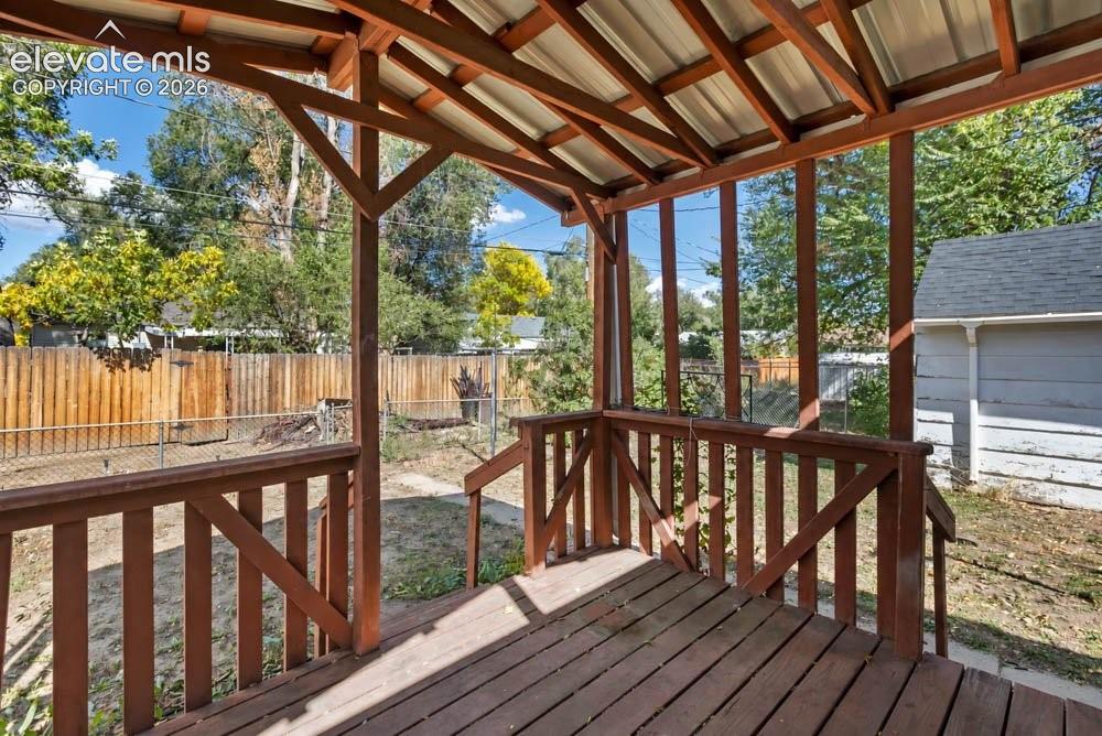 Image 35 of 45: Wood-decked covered porch with wood railing, supported by timber posts and
