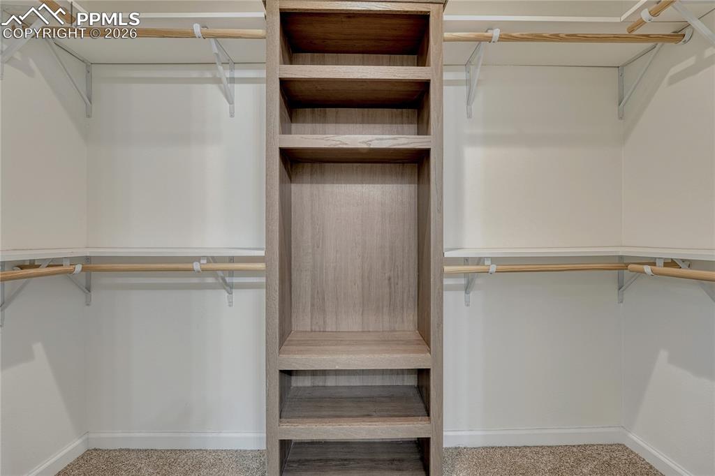 Image 30 of 48: Large primary walk-in closet with dual wrap around shelves and poles along 