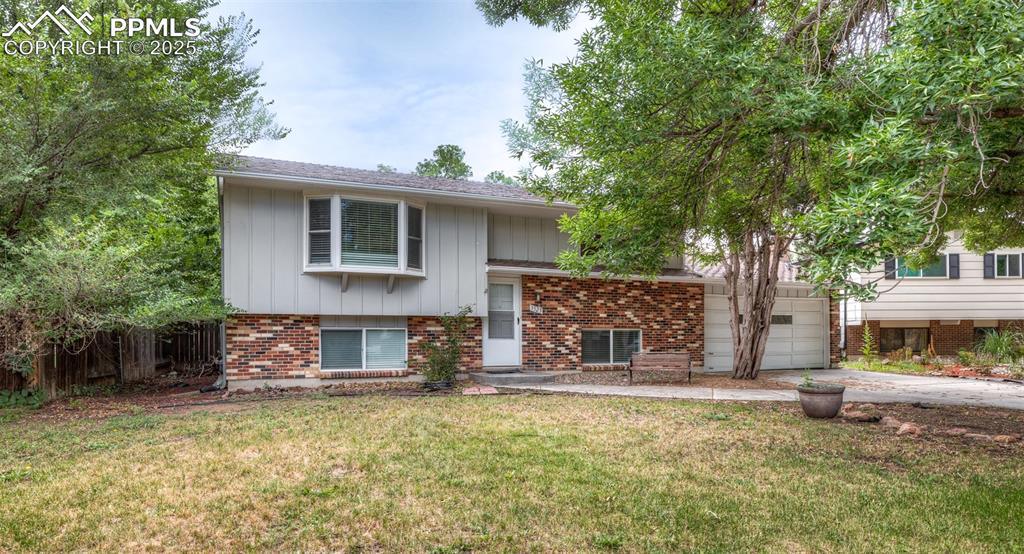 Caption: Bi-level home with board and batten siding, concrete driveway, brick siding, and an attached garage