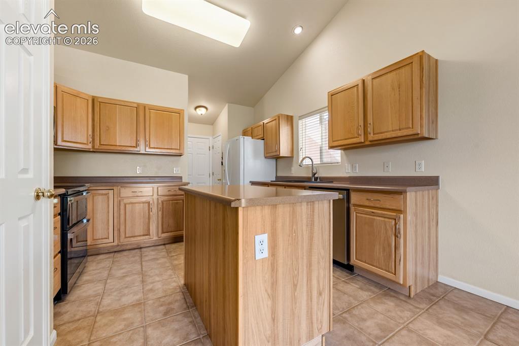 Image 10 of 33: Kitchen featuring vaulted ceilings, wood cabinetry, central island, solid s