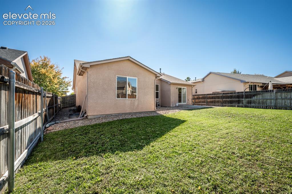 Image 30 of 33: Stucco exterior featuring a fenced backyard, gravel perimeter, and grass la