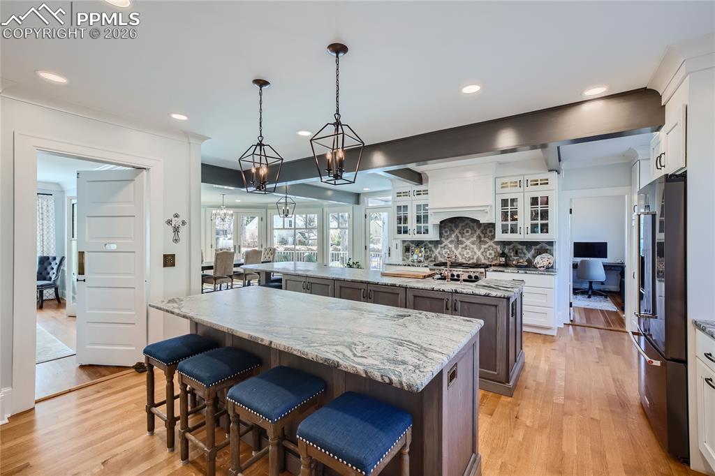 Image 10 of 49: Kitchen with white cabinets, backsplash, light wood flooring, two kitchen i