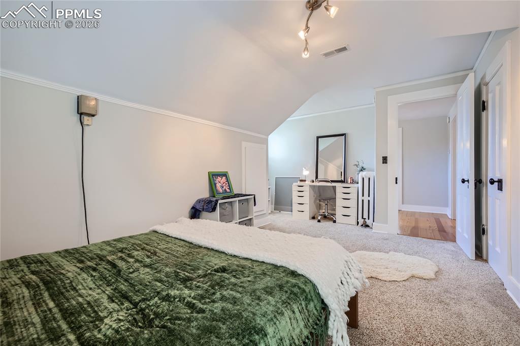 Image 43 of 49: Carpeted bedroom with vaulted ceiling, crown molding, radiator heating unit
