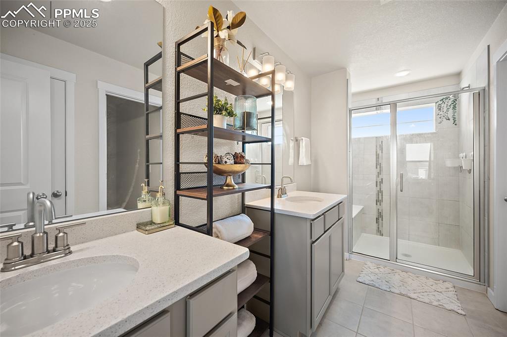 Image 9 of 41: Full bathroom with two vanities, a stall shower, and tile patterned floors