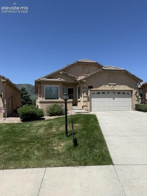 Caption: Stucco exterior residence featuring a two-car garage, concrete driveway, and front lawn