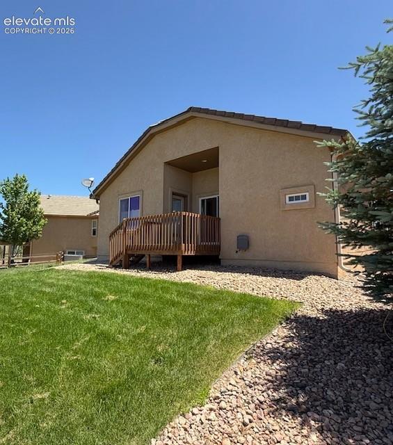 Image 3 of 24: Rear exterior featuring a tan stucco finish, private wood deck, and a cover
