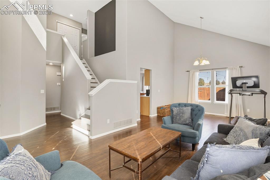 Image 12 of 34: Living room with high vaulted ceiling, stairway, wood finished floors, and