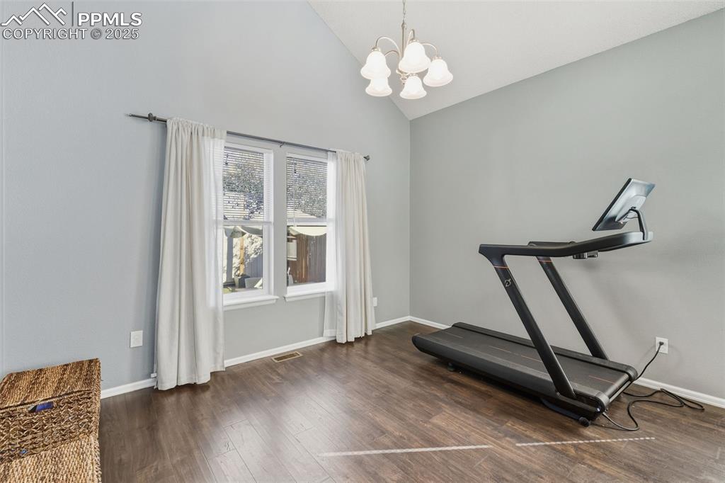 Image 22 of 34: Workout room with dark wood finished floors, a chandelier, and high vaulted