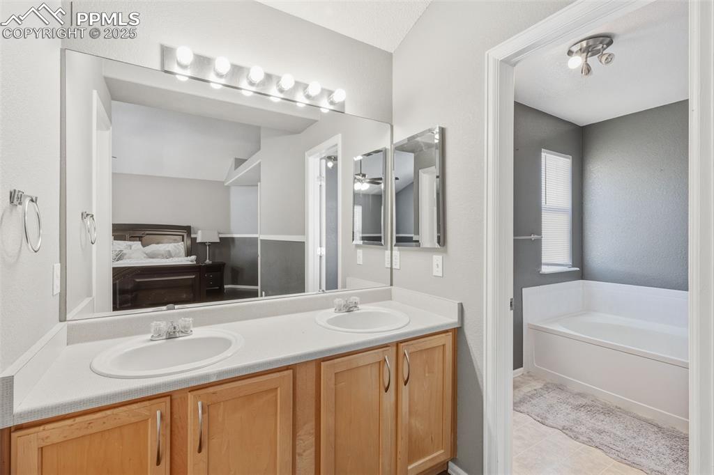 Image 25 of 34: Ensuite bathroom with double vanity, a bath, light tile patterned floors, a