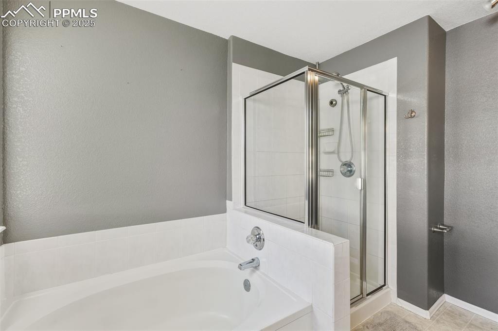 Image 26 of 34: Bathroom featuring a garden tub, a textured wall, a stall shower, and light