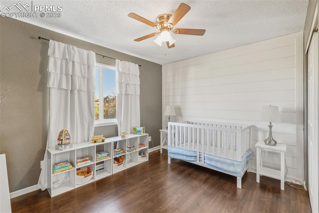 Image 29 of 34: Bedroom featuring a nursery area, a textured ceiling, dark wood-style floor
