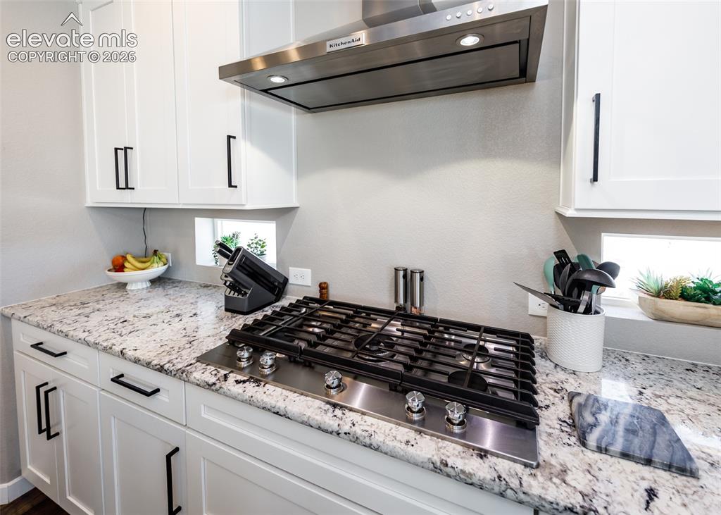 Image 15 of 50: White shaker-style cabinetry with matte black hardware, stainless steel gas