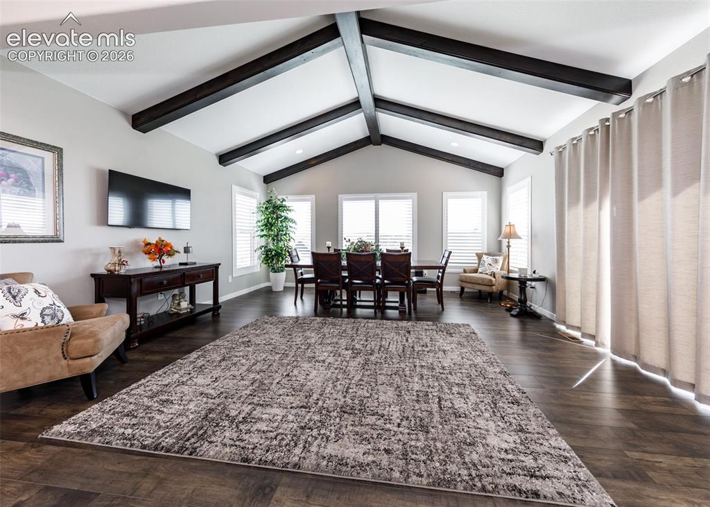 Image 17 of 50: Vaulted ceiling with exposed wood beams, multiple windows with white planta