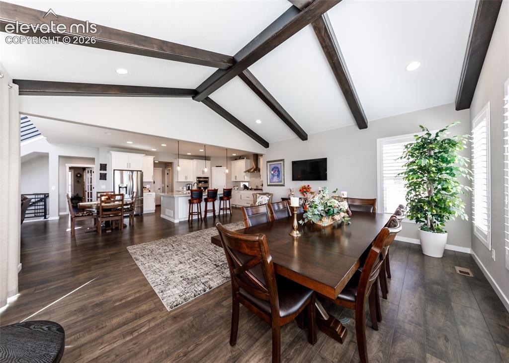 Image 19 of 50: Vaulted ceiling with exposed wood beams, wood-finish flooring, white kitche