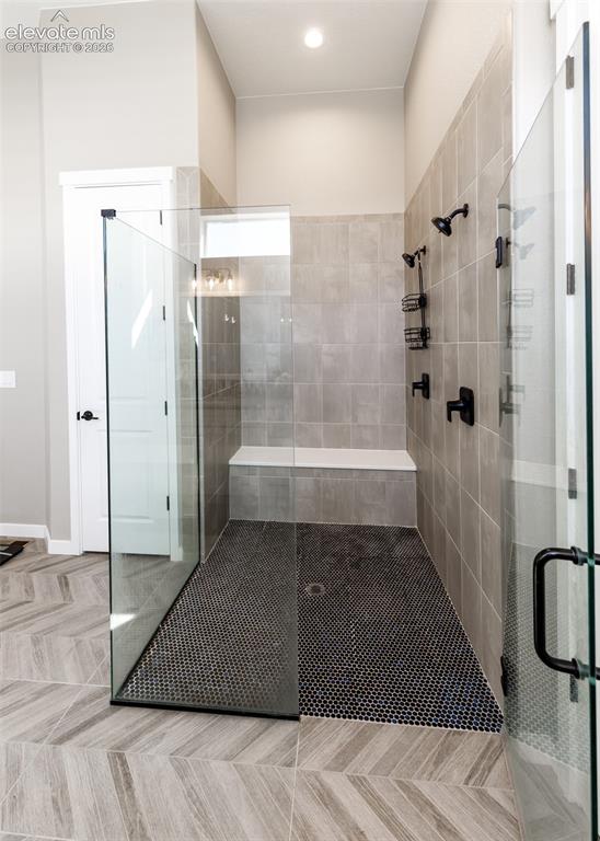 Image 27 of 50: Spacious walk-in shower featuring glass panels, a tiled bench, matte black 