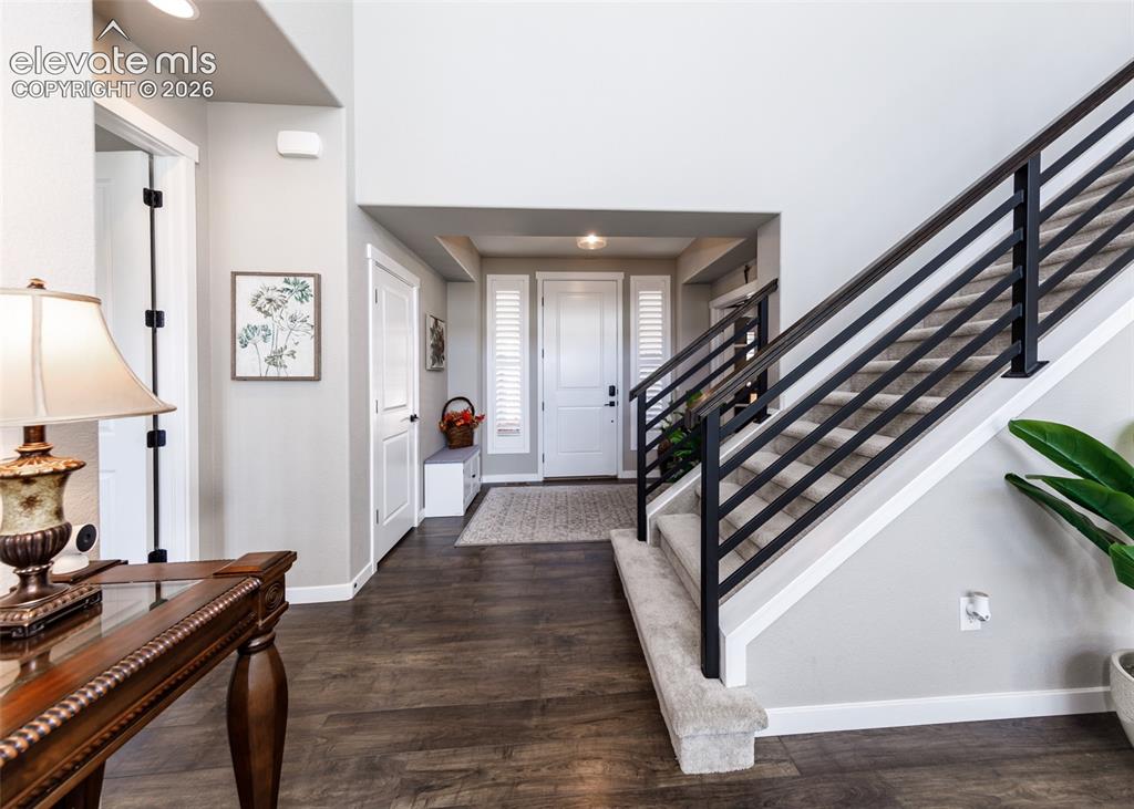 Image 6 of 50: Wood-finish flooring, staircase with black metal railings, carpeted stairs,