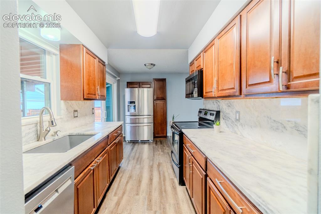 Image 10 of 33: Galley kitchen featuring wood-finish cabinetry, built in microwave, stainle